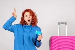 Mulher ao lado de mala de viagem segurando cartão com o Programa de Milhas Livelo