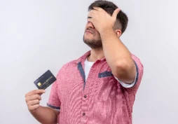 Homem com expressão de preocupação segurando cartão de crédito e levando a mão à testa, representando erro financeiro e impacto negativo no crédito.