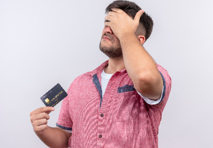 Homem com expressão de preocupação segurando cartão de crédito e levando a mão à testa, representando erro financeiro e impacto negativo no crédito.
