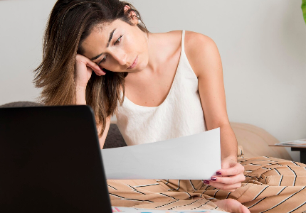 Mulher analisando contas e usando calculadora na mesa da cozinha, representando controle da fatura do cartão de crédito e organização financeira antes do fechamento da fatura.