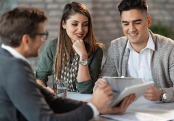 Casal sendo atendido por consultor financeiro analisando informações em tablet, representando avaliação de perfil financeiro e análise de comportamento pelo banco.