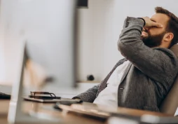 Homem com expressão de frustração sentado no escritório, cobrindo o rosto com a mão, representando problema financeiro após transferência bancária ou dinheiro não recebido.