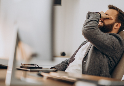 Homem com expressão de frustração sentado no escritório, cobrindo o rosto com a mão, representando problema financeiro após transferência bancária ou dinheiro não recebido.